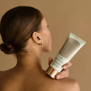 Silky Bronze Protective Suncare Cream for Body bottle shown in summer mood lighting  and being applied on model